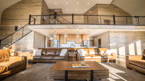 Spacious modern living room with leather sofas, wooden accents, and a lofted area, featuring bright natural light.